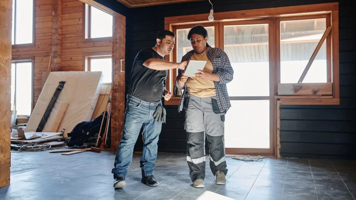Deux artisans du bâtiment en tenue de travail examinent des plans sur une tablette numérique dans un chantier, illustrant l'usage d'une application métier dans le Tarn.