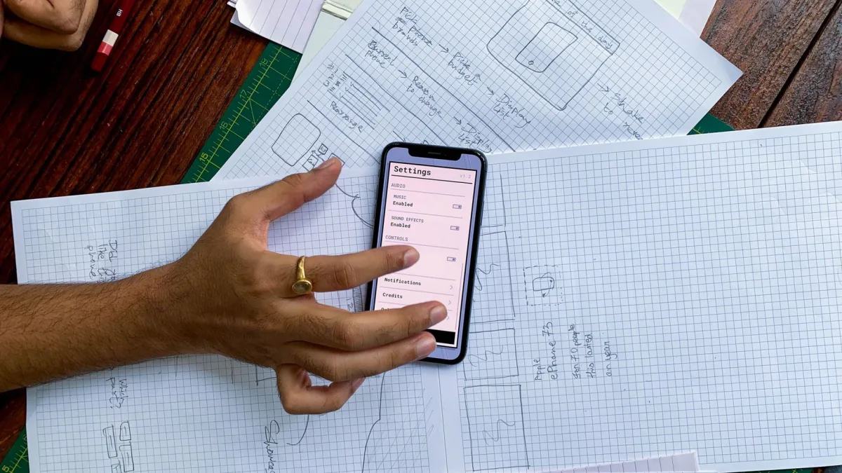 Une main manipule un smartphone posé sur des esquisses de maquettes applicatives lors de la conception d'un SaaS sur mesure dans les Pyrénées-Orientales.