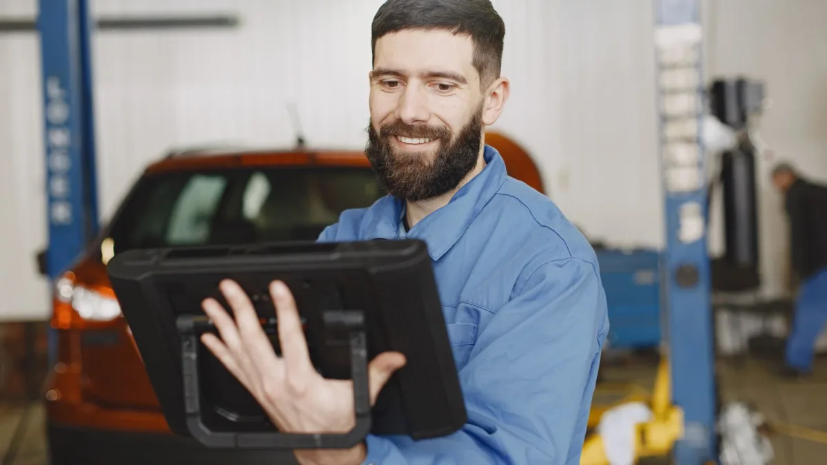 Mécanicien en bleu de travail utilisant une tablette tactile dans un garage devant un véhicule pour son application hors ligne dans les Pyrénées-Orientales.