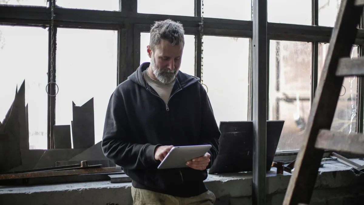 Un artisan consulte une tablette tactile debout dans son atelier de travail pour remplir ses fiches d'intervention à Perpignan.