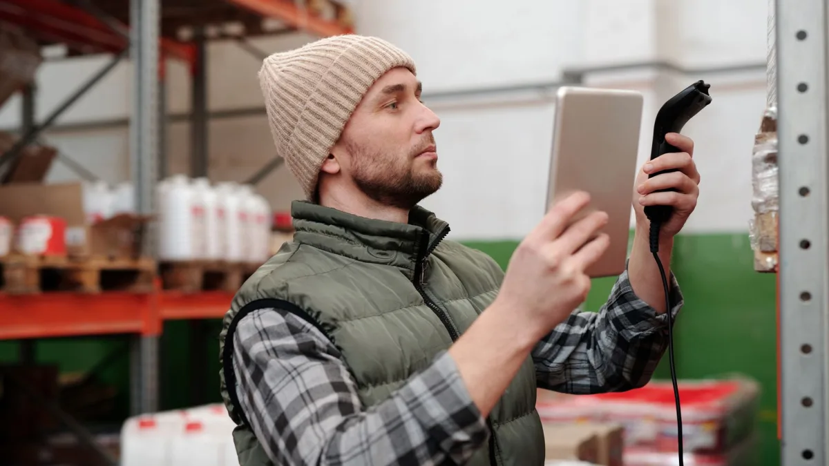 Un homme en gilet et bonnet utilise une tablette et un lecteur de code-barres dans un entrepôt pour la gestion d'un logiciel métier à Perpignan, illustration d'un article du blog d'EPREYN, développeur d'applications à Perpignan