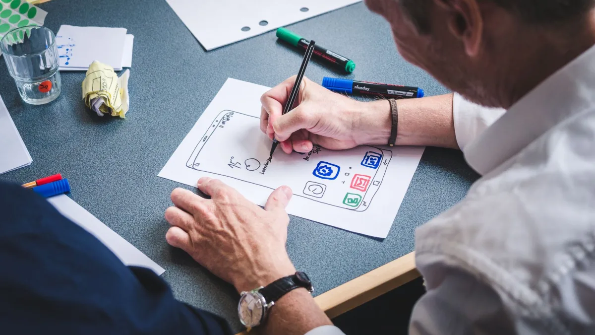 Un graphiste dessine la maquette d'une application mobile sur une feuille avec un feutre lors d'un projet de développement web à Perpignan.